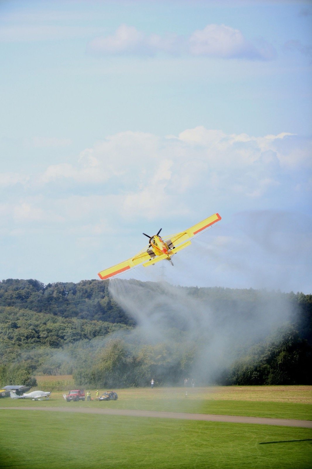 A yellow agricultural aircraft laying a spray swath low over a field