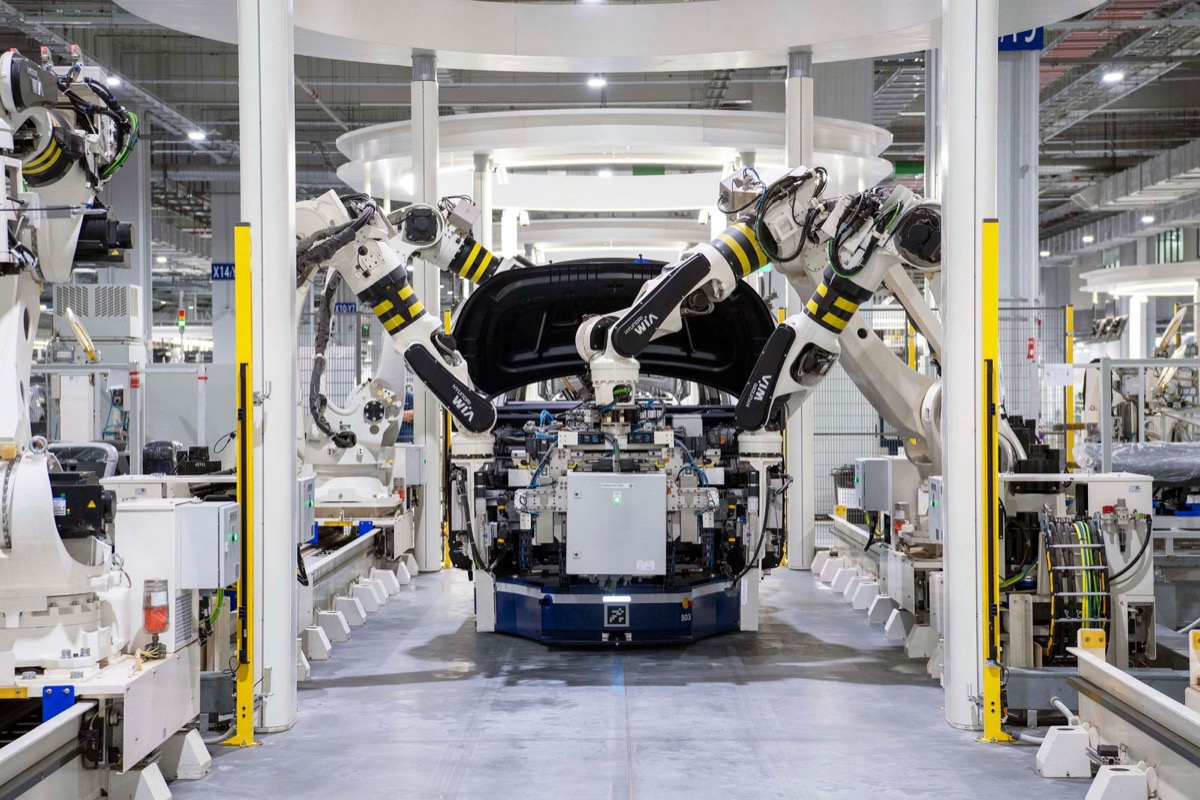 Multiple robots working over a vehicle body carried on an automated guided vehicle in a bright plant
