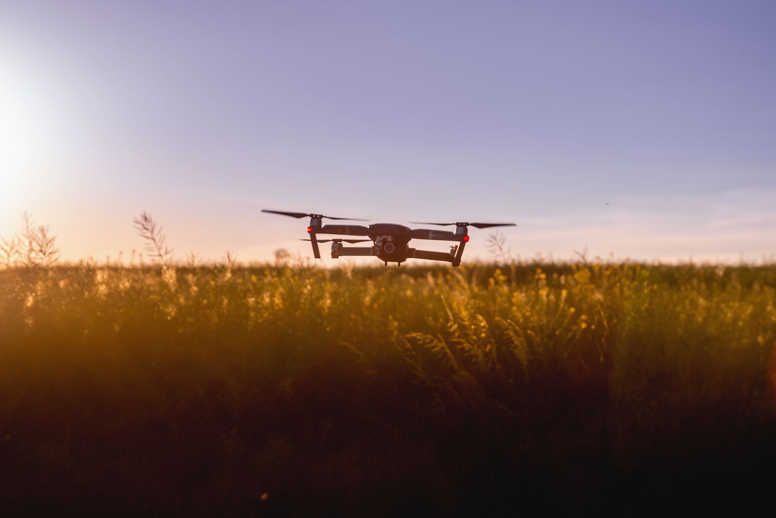 A small survey quadcopter hovering low over a field at golden hour