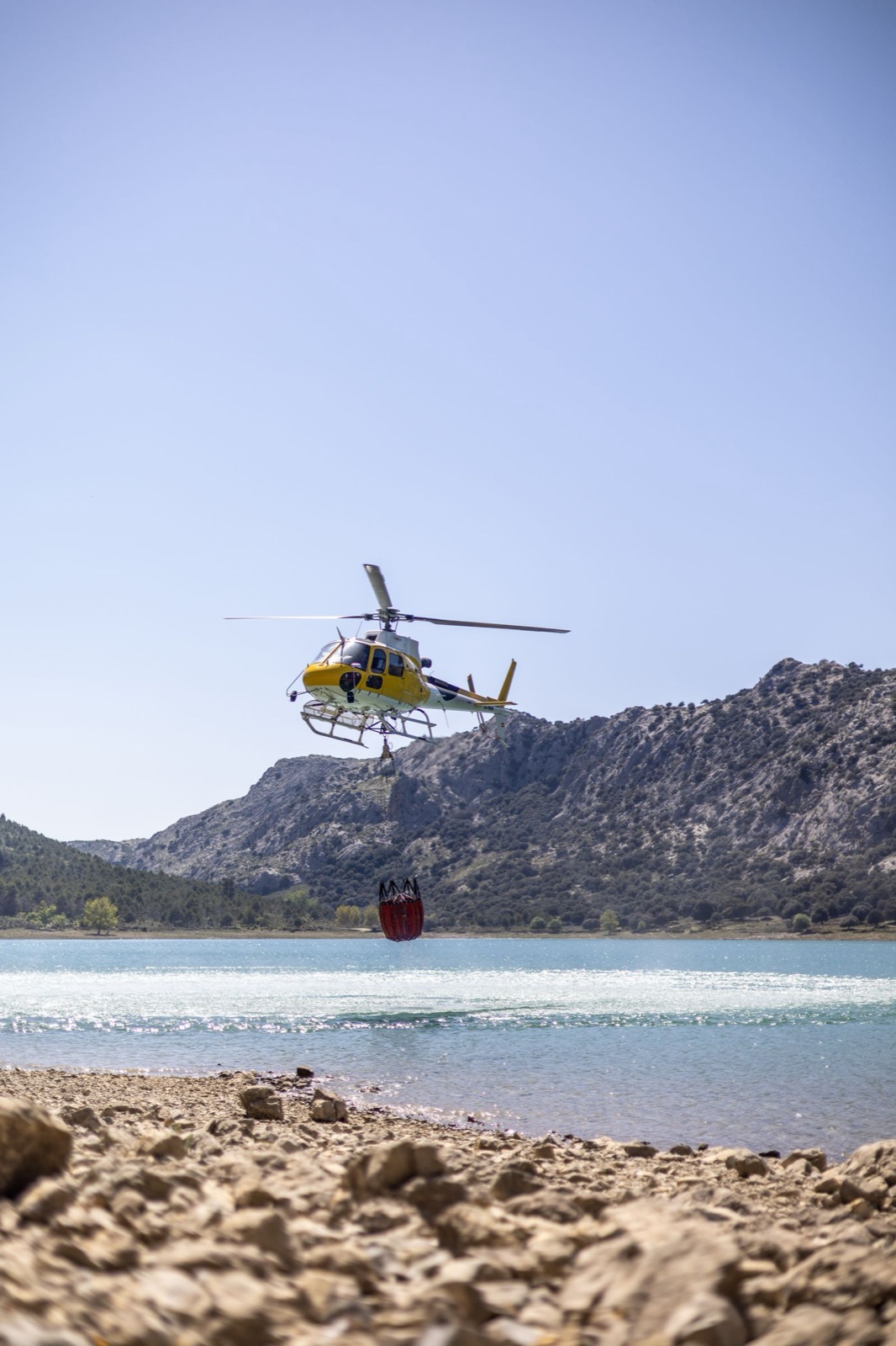 A utility helicopter dips a firefighting bucket into a mountain reservoir