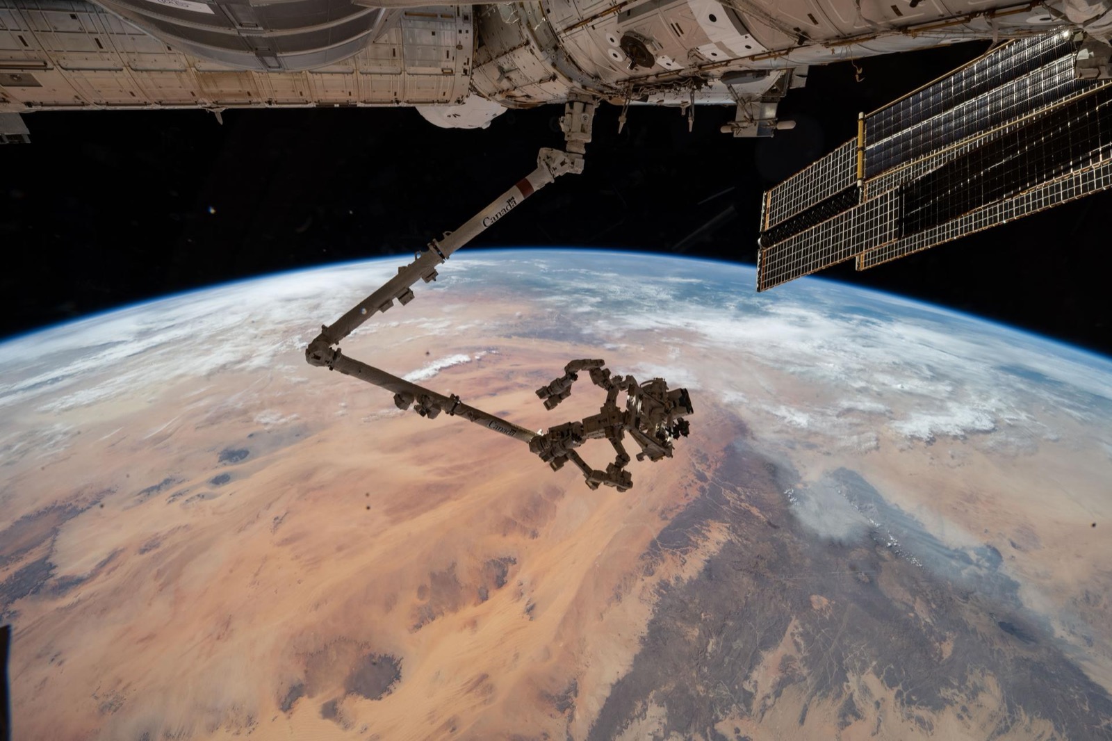 The Canadarm2 robotic arm with the Dextre robotic hand extended over Earth